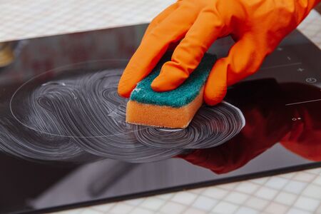 Close up hands cleaning kitchen glass ceramic electric surface with a sponge