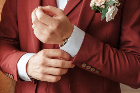Closeup of a groom in maroon suit correcting a sleeve.