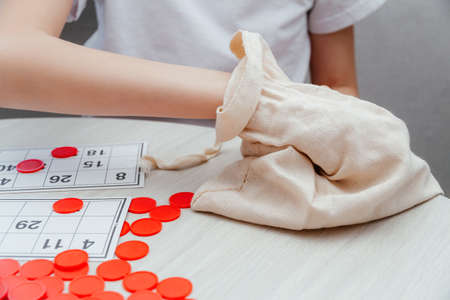 Girl takes out a wooden barrel with the number of the Russian lotto board game from the bag. Wooden...