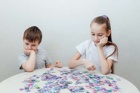 Sad boy and a girl collect a puzzle sitting at a table