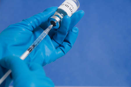 Hands in blue medical gloves drawing a syringe with covid-19 vaccine from a vial