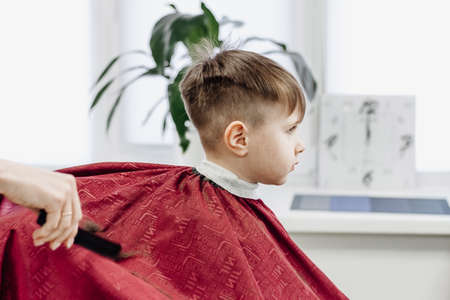 Portrait of male child at the barber shop to cut his hair. Little boy gets a haircut at a hair salon.の写真素材