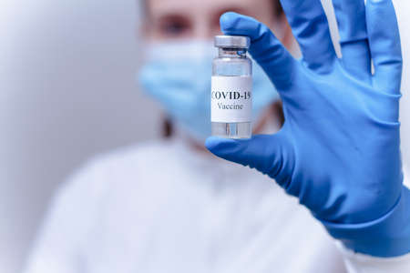 Female doctor wearing a protective mask holding a bottle of COVID-19 vaccineの写真素材