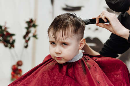 Close-up of woman hands grooming kid boy hair in barber shop.の写真素材