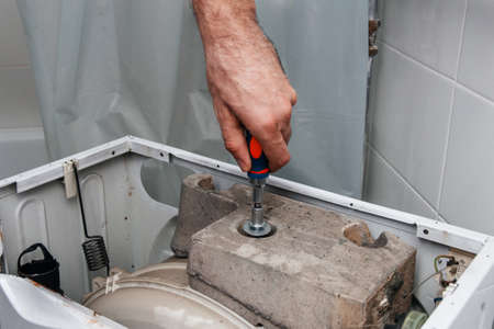 Handyman repairing a washing machine. The hands of a man disassemble the washing machine. Repair and dismantling of the washing machine. Close-upの写真素材