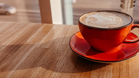 A red cappuccino cup on a cafe table against the background of a window in the rays of sunset light. Copy spaceの写真素材