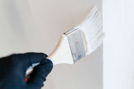 Close-up of a workers hand with a brush painting a wall with white paint.の写真素材