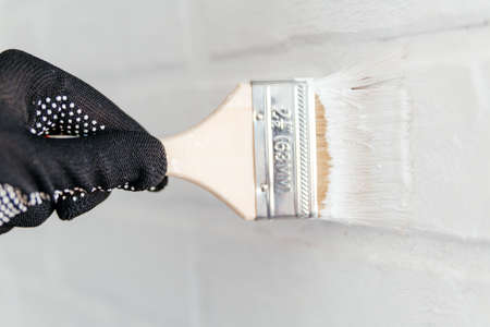 Close-up of a workers hand with a brush painting a brick wall with white paint.の写真素材