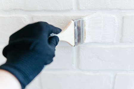 Close-up of a workers hand with a brush painting a brick wall with white paint.の写真素材