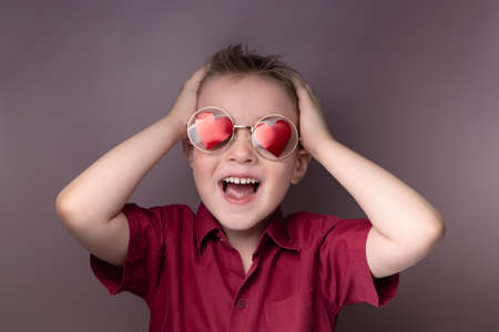 A smiling little boy in glasses with red hearts clutched his head with his handsの写真素材