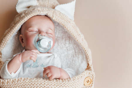Reborn a boy doll with a pacifier sleeps in a knitted beige envelope. copyspace.