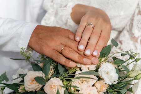 Hands of bride and groom with rings on wedding bouquet. Marriage concept.
