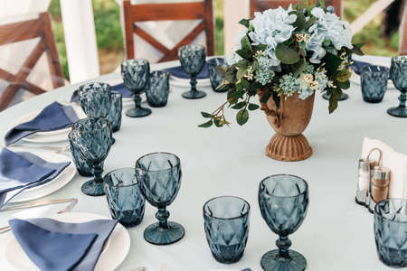 Blue glasses, plates and utensils on a festive table with flowers.