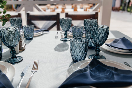Blue glasses, plates and utensils on a festive table with flowers.