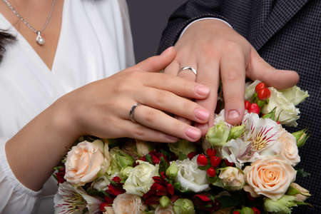 Hands of bride and groom with rings on wedding bouquet. Marriage conceptの写真素材