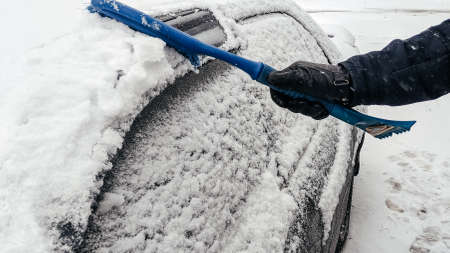 Man cleans car from snow with brush. Clean car window from snow. Winter windshield car cleaning.の写真素材