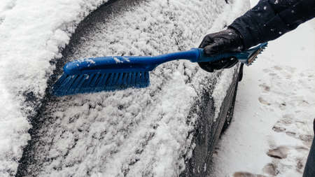 Man cleans car from snow with brush. Clean car window from snow. Winter windshield car cleaning.の写真素材
