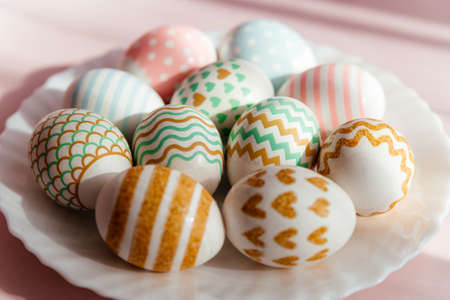 Easter eggs in pastel colors with a pattern lie on a white plate in the rays of the sun.