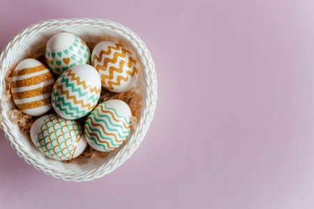 Colorful Easter eggs in a white basket on a pink background.
