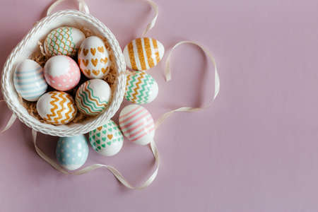 Easter eggs in pastel colors with a pattern in white basket on pink background.