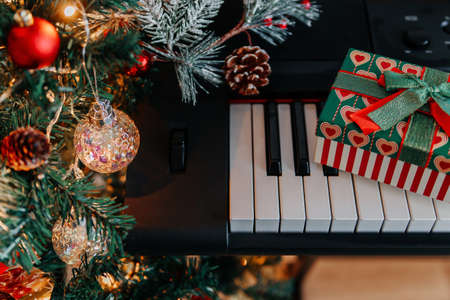 a Christmas gift on piano keys and a decorated Christmas tree with lightsの写真素材