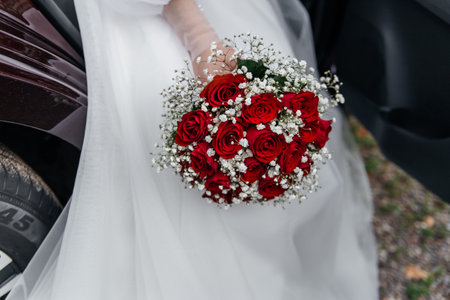 delicate wedding bouquet in the brides hand of red roses on the background of a white dress.の写真素材