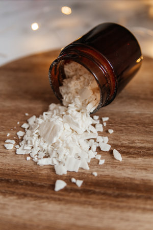 Flakes of white soy wax for making candles are scattered on a wooden stand from a glass jar, close-up. Ingredients for making homemade candlesの写真素材