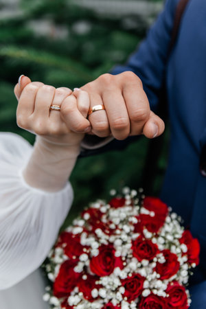 The intertwined fingers of the bride and groom, showing gold wedding rings on the background of the bouquet.の写真素材