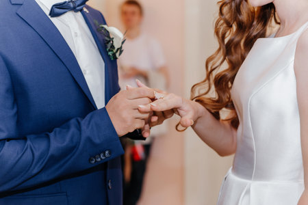 Groom putting golden ring on bride's finger during wedding ceremony. Hands with rings close upの写真素材