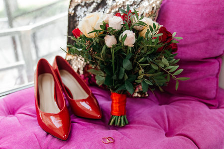 Red patent leather shoes of the bride near gold wedding rings and a bouquet of rosesの写真素材