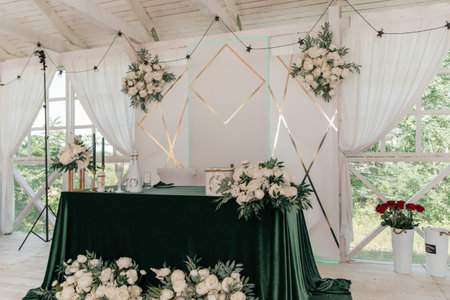 Wedding table of the bride and groom on the open veranda, decorated in green and white tones. White peonies with green leaves, green tablecloth and a casket on the table.の写真素材