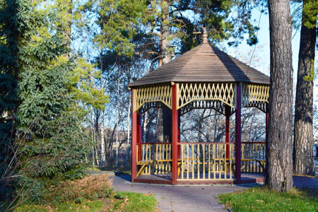a wooden arbor with red beams and a pattern stands in the middle of treesの写真素材