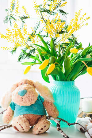 Spring bouquet of yellow tulips and mimosa in a vase and a plush dog.の写真素材