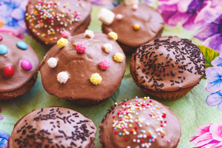 Homemade chocolate muffins with icing and colored sprinkles.