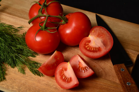 Red tomatoes on a board with dill and a knife on a black background