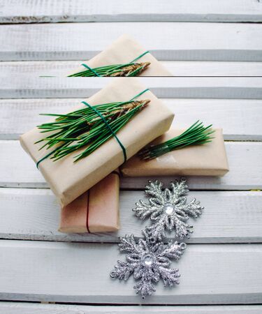 Christmas gifts in Kraft paper, with fir branches, with silver snowflakes, on a white wooden backgroundの写真素材