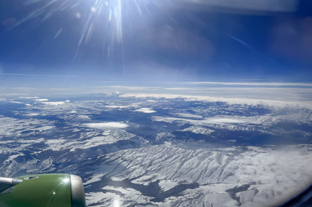 View of snow covered winter land and mountains from an airplane window.