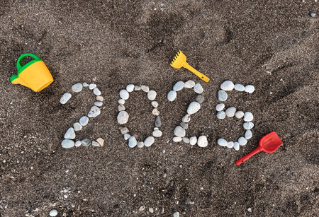 The inscription 2025 from stones on the beach. Childrens sand toys, watering can, scoop.