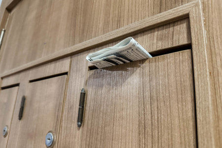 A close-up photo of a newspaper sticking out of a wooden mailbox in an apartment building.の写真素材