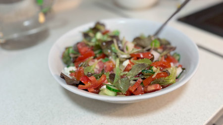 Close photo of white ceramic plate with natural fresh vegetable salad. Cucumbers, tomatoes, greens and white Greek feta cheese.の写真素材