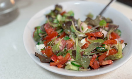Close photo of white ceramic plate with natural fresh vegetable salad. Cucumbers, tomatoes, greens and white Greek feta cheese.の写真素材