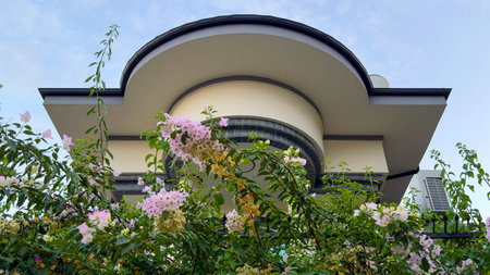 Photo of Architectural Facade and roof with Floral Greenery and Curved Design. A contemporary building surrounded by vibrant bougainvillea flowers under a serene sky.の写真素材