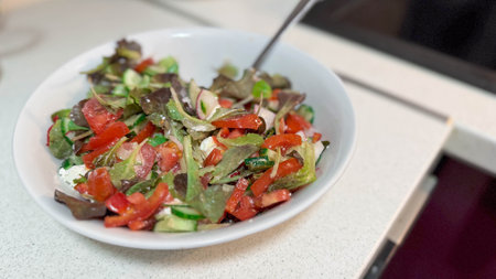 Close photo of white ceramic plate with natural fresh vegetable salad. Cucumbers, tomatoes, greens and white Greek feta cheese.の写真素材