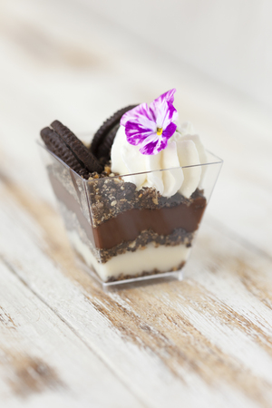 Trifle black and white chocolate with cookie. Decorated with a flower on old wooden white background. English traditional sweet dessert .の写真素材