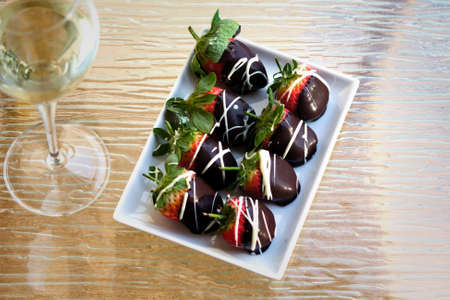 A plate of strawberries in chocolate on a glass surface with a glass of wineの写真素材