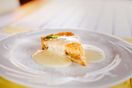 A piece of apple pie with vanilla sauce and mint leaf