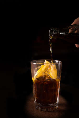 Barman prepares Cuba libre cocktail in a tall glass on the dark backgroundの写真素材