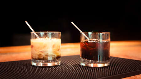 Black russian and white russian cocktails on the bar stand on rubber mat. Shallow DOF and marsala...