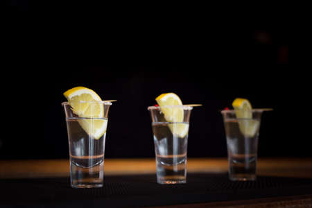 Three tequila shots with lemon on a bar ribber mat. Shallow DOF and toned