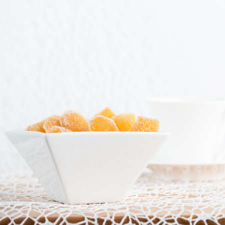Crystallized ginger root  in white porcelain bowl and cup of tea on the background. Shallow DOF. Close-up photo, squareの写真素材